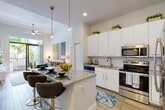 Located at 3400 Davie Rd in Davie, Florida, this well-appointed 3-bedroom, 3-bathroom residence offers a thoughtfully designed single-floor layout. The open-concept kitchen and living area serves as the heart of the home, featuring crisp white cabinetry, a granite-topped island with bar seating, pendant lighting, subway tile backsplash, and a full suite of stainless steel appliances. Light wood-style flooring flows throughout the main living areas, complementing the soaring ceilings and ceiling fan that enhance the airy ambiance. The living room opens directly to a private balcony through large sliding glass doors, offering serene views of lush tropical landscaping. Each bedroom is carpeted for comfort, with the primary suite offering a generous footprint, natural light from large windows, and access to a spa-like en-suite bathroom with a glass-enclosed walk-in shower and granite vanity. Additional bedrooms are well-sized, with tall ceilings that reinforce the sense of openness. Two dedicated closets provide practical storage. The bathrooms are finished with granite countertops, framed mirrors, and wood-look tile floors. Two dedicated closets add practical storage throughout the residence.