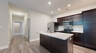 Located at 245 Market St in Charlestown, Indiana, this single-floor, 2-bedroom, 2-bathroom residence offers a thoughtfully arranged layout with modern finishes throughout. The kitchen serves as the heart of the home, featuring rich dark cabinetry, stainless steel appliances, light granite countertops, and a central island with a built-in sink — ideal for both cooking and casual dining. Wood-look luxury vinyl flooring runs through the main living areas, adding warmth and durability. The two bedrooms are carpeted in neutral tones, providing a comfortable and quiet retreat. The primary bedroom is generously sized and includes access to a dedicated closet. Both bathrooms are finished with wood-look flooring, clean white surrounds, and dark vanity cabinetry with contemporary fixtures — one featuring a tub/shower combination and the other a walk-in shower. A utility room adds practical storage and functionality to the floor plan. Neutral wall tones and recessed lighting throughout create a bright, cohesive atmosphere. The layout is efficiently organized, making excellent use of the available space while maintaining a clean, modern aesthetic suitable for everyday living.