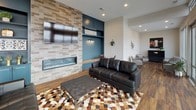 Located at 115 Dayton St in Hamilton, Ohio, this thoughtfully designed single-floor space offers a seamless blend of modern aesthetics and functional living. The open-concept layout is anchored by rich hardwood flooring that runs throughout, creating a warm and cohesive foundation for the entire space.

The main living area is a showstopper, featuring an expansive wall of floor-to-ceiling sliding glass doors and clerestory windows that flood the interior with natural light and provide sweeping views of the surrounding neighborhood and skyline. These doors open directly onto a spacious outdoor terrace furnished for lounging, extending the usable area and blurring the line between indoors and out.

A striking accent wall clad in stacked stone houses a sleek linear fireplace below a wall-mounted television, flanked by bold teal-painted built-in shelving that adds a vibrant pop of color and architectural interest. Adjacent to the main seating area, a cozy nook with matching teal built-ins offers an intimate space for smaller gatherings or quiet retreat.

The kitchen area, visible along the back wall, features teal cabinetry, pendant lighting, and modern appliances, maintaining the consistent design language found throughout. Additional seating areas with mid-century modern furnishings provide versatile spaces suited for both social and private use. The overall ambiance is contemporary, inviting, and rich with carefully curated design details.