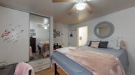 This single-floor residential space is located along Harris Alley in Eugene, Oregon, offering a comfortable and functional bedroom layout. The room features light wood-tone flooring throughout, which lends a clean, warm aesthetic to the space. A ceiling fan with a built-in light fixture is centrally positioned overhead, providing both ventilation and ambient lighting.

The bedroom is anchored by a spacious sleeping area accommodating a large bed, complemented by a set of sliding mirrored closet doors that visually expand the room and offer generous storage. A built-in desk area along one wall provides a dedicated workspace, paired with additional drawer storage, making the room well-suited for both rest and productivity. Dark-toned dresser units add contrast to the lighter walls and flooring.

Natural light filters into the room through windows fitted with horizontal blinds, offering privacy while still brightening the interior. A decorative round mirror adorns one wall, adding a stylistic touch to the space. An en-suite or adjacent room is accessible through a doorway, visible from multiple angles within the bedroom.

Wall-mounted framed artwork and thoughtful decorative accents contribute to the room's personalized, lived-in character. The overall layout is efficient and well-organized, making effective use of the available space in this Eugene, Oregon residence.