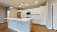 Located at 4455 Winder Dr in Dublin, OH, this well-appointed two-bedroom, two-bathroom residence offers a thoughtfully designed single-floor layout. The kitchen is a standout feature, showcasing floor-to-ceiling white shaker cabinetry, a subway-tile backsplash, and a large center island with a white quartz countertop and integrated sink. A full suite of stainless steel appliances — including a refrigerator, range, microwave, and dishwasher — completes the space. Warm hardwood-style flooring flows throughout the kitchen and living areas, creating a cohesive, modern aesthetic. The living room is bright and airy, benefiting from an expansive wall of large windows that invite abundant natural light and outdoor views. Both bedrooms feature plush carpeting and neutral tones; the primary bedroom is generously sized and includes access to a dedicated walk-in closet with wire shelving for ample storage. The bathrooms are finished with wood-look flooring, white cabinetry, and a glass-enclosed walk-in shower. Throughout the residence, clean lines, neutral gray walls, and white trim contribute to a contemporary and functional living environment.