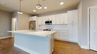 Located at 4455 Winder Dr in Dublin, OH, this well-appointed two-bedroom, two-bathroom residence offers a thoughtfully designed single-floor layout. The kitchen is a standout feature, showcasing floor-to-ceiling white shaker cabinetry, a subway-tile backsplash, and a large center island with a white quartz countertop and integrated sink. A full suite of stainless steel appliances — including a refrigerator, range, microwave, and dishwasher — completes the space. Warm hardwood-style flooring flows throughout the kitchen and living areas, creating a cohesive, modern aesthetic. The living room is bright and airy, benefiting from an expansive wall of large windows that invite abundant natural light and outdoor views. Both bedrooms feature plush carpeting and neutral tones; the primary bedroom is generously sized and includes access to a dedicated walk-in closet with wire shelving for ample storage. The bathrooms are finished with wood-look flooring, white cabinetry, and a glass-enclosed walk-in shower. Throughout the residence, clean lines, neutral gray walls, and white trim contribute to a contemporary and functional living environment.