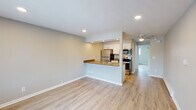 This single-floor unit offers a clean, modern layout designed for comfortable everyday living. The open-concept living and kitchen area forms the heart of the space, where light-toned luxury vinyl plank flooring runs seamlessly throughout, enhancing the bright, airy atmosphere created by recessed ceiling lighting and neutral warm-gray walls with crisp white trim.

The kitchen is thoughtfully equipped with stainless steel appliances, including a refrigerator, electric range, over-the-range microwave, and dishwasher. White shaker-style cabinetry with brushed nickel hardware lines the walls, complemented by a dual-basin stainless steel sink with a contemporary pull-down faucet. A peninsula counter with a dark countertop serves as a natural divider between the kitchen and the living area, providing additional prep space and a casual seating option.

The living area is generously proportioned and includes a ceiling fan, offering flexible use as a lounge or dining space. The bedroom features a wall-mounted air conditioning unit, a baseboard heater, and a window that allows natural light to fill the room.

The bathroom is clean and functional, outfitted with a full soaking tub and shower combination, a single-sink vanity with white cabinetry, and brushed nickel fixtures throughout. The overall design is understated and move-in ready, making the most of every square foot.
