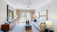 Located at 1000 Creekview Cir in Cranberry Township, Pennsylvania, this single-floor residence offers a thoughtfully designed layout with a refined aesthetic throughout. The living room serves as the centerpiece of the space, featuring crown molding, plush carpeting, and a ceiling fan that enhances the airy atmosphere. A pair of French doors floods the room with natural light and opens directly onto a private balcony, offering views of the surrounding community and pool area. A warm wood media console anchors one wall, while a tufted sofa and contemporary coffee table complete the welcoming setting. The kitchen is outfitted with dark cabinetry, granite countertops, stainless steel appliances, and hardwood-style flooring. A peninsula with pendant lighting provides bar seating and serves as a natural divide between the kitchen and living areas. The bedroom is a tranquil retreat, featuring plush carpeting, a ceiling fan, and a large window that invites natural light and outdoor views. Crown molding and neutral tones lend the room a polished finish. A spacious walk-in closet with wire shelving offers generous storage. The overall ambiance of the space is clean, modern, and well-appointed, making it an inviting and functional home.