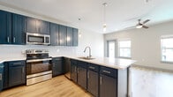 Located at 2422 S Carrier Pkwy in Grand Prairie, TX, this well-appointed one-bedroom, one-bathroom unit offers a thoughtfully designed layout with modern finishes throughout. The open-concept kitchen and living area serves as the heart of the space, showcasing bold navy-blue shaker cabinets, a white subway tile backsplash, stainless steel appliances, and a spacious peninsula island with a light quartz countertop and pendant lighting overhead. Light hardwood-style flooring flows throughout the main living areas, lending warmth and continuity to the space. The living area benefits from natural light via a large window and glass door, creating a bright, welcoming atmosphere. The bedroom features soft carpeting underfoot, multiple windows with outdoor views, a ceiling fan, and access to a dedicated closet with built-in shelving and a hanging rod for ample storage. The bathroom is finished with clean, modern tile and includes a walk-in shower with a glass enclosure. Conveniently, a stacked washer and dryer unit is also accommodated within the unit. The overall design palette of neutral walls, gray accents, and contemporary hardware creates a cohesive and move-in-ready aesthetic well-suited for comfortable everyday living.