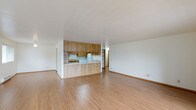 This single-floor unit is designed with an open, functional layout that connects the living, dining, and kitchen areas into one cohesive space. Light wood laminate flooring runs throughout the main living areas, lending a warm, consistent feel across the unit.

The kitchen is positioned centrally and features a peninsula with a wood-toned cabinet base, providing both prep space and a natural division between the kitchen and living area. Warm oak cabinetry lines the walls, offering generous upper and lower storage, while white appliances — including a refrigerator, electric range, and dishwasher — complete the setup. Light-toned countertops and tile-style flooring finish the kitchen interior.

The living area is notably spacious and bright, with two sliding glass doors fitted with vertical blinds opening to an outdoor balcony. An additional window allows further natural light to fill the room.

The bathrooms include a full bath with a tub-shower combination, single vanity, and tile-style flooring, as well as a larger bathroom featuring a dual-sink vanity with oak cabinetry and lighted mirrors. A dedicated dressing area with shelving and a vanity sink provides additional functionality. The overall ambiance is clean, neutral, and move-in ready.