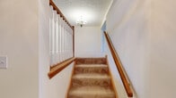 This three-floor home offers a well-organized layout across its levels, each serving a distinct functional purpose. The main level showcases an open floor plan with notably high ceilings, visible from the overhead view that also reveals a striking arched window at the entry, flooding the space with natural light. The kitchen is equipped with warm honey-toned wood cabinetry, granite-look laminate countertops, a double stainless steel sink, and a full appliance suite including an electric range with overhead ventilation. A convenient half bathroom with hardwood-style flooring and a wood-toned vanity is also found on this level. Carpeted stairs with polished wood banisters and a decorative chandelier connect the floors with classic charm. The upper level hosts carpeted bedrooms featuring neutral walls, natural window light, and closets with built-in shelving. A full bathroom on this level includes a tub-shower combo, wood vanity, and hardwood-style flooring. The lower level contains an unfinished basement with painted concrete block walls, exposed wood-beam ceilings, and utility infrastructure, offering versatile potential. An attached two-car garage with an automatic opener and overhead lighting completes the home.