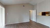 This single-floor home offers a thoughtfully designed layout with a blend of practical finishes and comfortable living spaces throughout. The open living area immediately impresses with its vaulted ceilings, which lend a spacious, airy feel to the room. Rich wood-look hard flooring extends across the main living spaces, complemented by neutral gray walls and a ceiling fan with integrated lighting. A pass-through connects the living area to the kitchen, which features dark espresso cabinetry, granite-style countertops, black appliances including a refrigerator and range, and direct access to a dedicated laundry area housing side-by-side washer and dryer units. The bedrooms are carpeted for added comfort, each equipped with ceiling fans and window blinds that allow for natural light control. One bedroom benefits from large windows that invite ample natural light. The bathrooms are finished with dark vanity cabinetry, granite countertops, and white tile tub-shower surrounds with brushed nickel fixtures and hardware. The overall ambiance of the home is clean, neutral, and move-in ready, with consistent finishes throughout that create a cohesive and functional living environment.