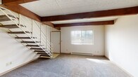 Located at 6364 Rippey Cir in Reynoldsburg, Ohio, this two-floor home offers a functional and practical layout with several notable architectural details. The main living area on the first floor makes an immediate impression with its rich, dark wood exposed beams running across the textured ceiling, adding warmth and character to the space. Soft carpeting covers the generously sized living area, which is brightened by a front-facing window with blinds and features a baseboard heating unit. A staircase with metal railings leads to the upper level, and an entry door provides convenient access from the main floor. The open layout connects the living area to the kitchen, which is equipped with warm wood cabinetry, light stone-patterned countertops, a stainless steel sink, and a white electric range with an overhead exhaust hood. In-unit washer and dryer hookups are also conveniently located adjacent to the kitchen. Upstairs, the bedrooms are carpeted and well-lit by windows overlooking the surrounding greenery, each outfitted with a ceiling fan. The bathroom is clean and functional, featuring tile flooring, a full tub-shower combination, a wide vanity with an integrated sink, and a large mirror with overhead lighting. Throughout the home, a neutral color palette and practical finishes create a comfortable, move-in-ready environment.