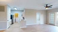 This single-story residence at 11414 Chriswick House On in Raleigh, NC offers a well-designed, open layout with consistent finishes throughout. Light-toned luxury vinyl plank flooring runs through the main living areas, complemented by neutral warm-gray walls, white trim, and crown molding that lend the space a clean, polished character.

The living area is spacious and open, featuring a ceiling fan, access to an outdoor patio through sliding glass doors, and a seamless flow into the kitchen and dining spaces. The kitchen is outfitted with white shaker-style cabinetry accented by matte black hardware, quartz countertops, a white subway tile backsplash, and stainless steel appliances including a range, over-the-range microwave, and refrigerator. A peninsula provides additional prep and serving space.

The dining area features a pendant light fixture and a six-panel door leading to additional rooms. Bedrooms are carpeted for comfort, each equipped with ceiling fans and windows offering outdoor views. The bathrooms feature light wood-look flooring, white vanities with matte black fixtures, and tiled tub-shower combinations. A dedicated laundry room houses a full-size washer and dryer with overhead wire shelving for added storage.