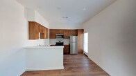 Located at 671 Woodward in San Marcos, Unit #8 Upstairs is a single-floor residence that combines functional design with a clean, neutral aesthetic throughout. The layout, as seen in the floor plan, offers a well-organized arrangement of living, kitchen, bedroom, and bathroom spaces connected by a logical flow.

The kitchen is a standout feature, showcasing warm-toned wood cabinetry that extends to the ceiling for generous storage capacity. Stainless steel appliances — including a gas range, built-in microwave, and full-size refrigerator — provide a modern contrast against the white countertops. A peninsula with a sink adds workspace and separates the kitchen from the adjoining living area, which features rich, dark hardwood-style flooring and multiple windows that invite natural light. The open living space offers a generous, flexible footprint suitable for varied furniture arrangements.

The bedrooms are carpeted in neutral tones and feature windows that bring in additional natural light, creating comfortable, well-lit retreats. The unit includes two bathrooms: one with a tub-shower combination enclosed in a sliding glass door, and another with a dedicated walk-in shower, also with a sliding glass enclosure. Both bathrooms maintain a clean, light palette with windows above the shower areas for ventilation and natural light.