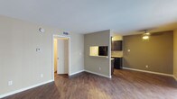This single-floor unit is thoughtfully laid out across a cohesive, open floor plan with a warm, neutral color palette throughout. The living area is spacious and features rich, dark wood-style flooring that extends through the main living spaces, complemented by neutral beige walls and clean white trim. Vertical blinds and a sliding glass door allow natural light to fill the room while providing outdoor access.

The galley-style kitchen is efficiently designed with dark espresso cabinetry lining both sides, light granite-style countertops, and black appliances including a range and refrigerator. A pass-through window connects the kitchen to the living area, enhancing the sense of openness between spaces.

The bedrooms are carpeted for comfort and each features a ceiling fan with integrated lighting. One bedroom benefits from a large sliding glass door with vertical blinds, allowing abundant natural light and outdoor access, while a second bedroom includes a standard window with blinds.

The bathroom presents a streamlined corridor layout with dark cabinetry, a granite-style vanity countertop, a single undermount sink, and a well-lit mirror. Wood-style flooring continues through the hallway, tying the spaces together with a consistent, cohesive aesthetic throughout the unit.