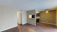 This single-floor unit is thoughtfully laid out across a cohesive, open floor plan with a warm, neutral color palette throughout. The living area is spacious and features rich, dark wood-style flooring that extends through the main living spaces, complemented by neutral beige walls and clean white trim. Vertical blinds and a sliding glass door allow natural light to fill the room while providing outdoor access.

The galley-style kitchen is efficiently designed with dark espresso cabinetry lining both sides, light granite-style countertops, and black appliances including a range and refrigerator. A pass-through window connects the kitchen to the living area, enhancing the sense of openness between spaces.

The bedrooms are carpeted for comfort and each features a ceiling fan with integrated lighting. One bedroom benefits from a large sliding glass door with vertical blinds, allowing abundant natural light and outdoor access, while a second bedroom includes a standard window with blinds.

The bathroom presents a streamlined corridor layout with dark cabinetry, a granite-style vanity countertop, a single undermount sink, and a well-lit mirror. Wood-style flooring continues through the hallway, tying the spaces together with a consistent, cohesive aesthetic throughout the unit.