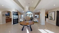 Located at 7901 N Cortaro Rd in Marana, Arizona, this single-story clubhouse serves as the welcoming community hub for The Springs at Continental Ranch. The grand entrance immediately impresses with soaring vaulted ceilings, an elegant arched transom window above French doors, and a geometric pendant chandelier that anchors the space with architectural distinction. Light-toned flooring runs throughout, reflecting generous natural light streaming in from multiple windows fitted with warm woven shades.

The main lounge area is thoughtfully furnished with a navy blue sofa, white accent chair, and a rustic wood coffee table, creating a relaxed yet polished gathering space. A large round wooden table at the center of the entry zone provides an additional focal point. Decorative wall art and sculptural accents lend a curated, contemporary desert aesthetic to the interiors.

Toward the rear, a café-style workspace area features industrial-inspired pendant lighting, a textured accent wall with a reclaimed wood aesthetic, built-in countertop with a sink, and mixed seating including bar-height tables — ideal for residents seeking a functional lounge or co-working environment. Striking dark-stained sliding barn doors define this zone while maintaining an open, connected flow to the rest of the clubhouse, reinforcing the space's blend of modern and rustic design sensibilities.
