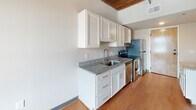 Located at 12 S 17th St in Richmond, VA, this single-floor unit masterfully combines historic industrial character with contemporary updates. The living area is defined by striking exposed brick walls, original heavy timber wood-beam ceilings, and warm hardwood flooring that together create an authentic loft-style ambiance. Large windows set within the brick allow natural light to fill the space while offering views of the surrounding Shockoe Bottom neighborhood.

The kitchen features white shaker-style cabinetry, granite countertops, a stainless steel sink, and a full suite of stainless steel appliances including a refrigerator, electric range, and dishwasher. Hardwood flooring continues throughout the kitchen, which also includes a louvered-door closet for additional storage.

The bedroom continues the building's historic character with exposed brick, wood-beam ceilings, and a large arched window, while plush carpeting underfoot adds comfort. Two bathrooms serve the unit: one features a granite-topped vanity with an LED-framed mirror and a stacked in-unit washer/dryer, while the second offers a full soaking tub with shower. Clean white walls throughout provide a bright, modern contrast to the rich historic architectural details.