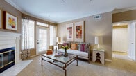 This single-floor residence offers a thoughtfully designed layout with distinct living spaces that blend comfort and functionality. The living room serves as the heart of the home, anchored by a classic white-mantled fireplace and framed by large windows with shuttered blinds that invite generous natural light. Crown molding accents the ceiling, adding an elegant architectural detail, while warm taupe walls create a cohesive and inviting ambiance throughout. A glass-topped coffee table and direct access to an outdoor area via a French door enhance the room's open, airy feel.

The kitchen is well-equipped with rich dark wood cabinetry, white countertops, and white appliances including an electric range with over-the-range microwave, providing ample functionality and storage for everyday use. Light tile flooring gives the kitchen a clean, practical finish.

The bathroom is bright and spacious, featuring an extended white vanity with dual sinks, a large mirror, recessed lighting, and a glass-enclosed shower, offering a clean and functional retreat. Tile flooring throughout completes the polished look.

The bedrooms are carpeted and finished with the same warm neutral palette, offering a calm and restful atmosphere. A hallway connecting the secondary bedroom provides convenient access to an adjacent bathroom, ensuring a practical and well-organized floor plan overall.