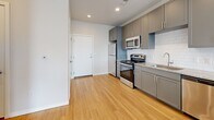 Located at 3165 S Quari St in Aurora, CO, this well-appointed one-bedroom, one-bathroom residence offers a thoughtfully designed single-floor layout. The open-concept living, dining, and kitchen area creates a bright, cohesive space ideal for everyday living and entertaining. The kitchen stands out with sleek gray shaker cabinetry, granite countertops, a classic white subway tile backsplash, stainless steel appliances including a range, microwave, and refrigerator, and warm hardwood-style flooring that flows throughout the main living area. Pendant lighting above the kitchen peninsula adds a modern touch, while large windows invite ample natural light into the living space. The bedroom features soft carpeting, generous closet space, and oversized windows that frame open outdoor views, flooding the room with sunlight. The full bathroom is clean and functional, offering a tub/shower combination with crisp white surrounds and hardwood-style flooring. Additional highlights include three closets for abundant storage and a dedicated in-unit laundry area for everyday convenience. The overall aesthetic is modern and neutral, with a cohesive color palette that creates a calm, welcoming ambiance throughout.