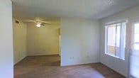 This single-floor space offers a straightforward, open layout that connects the living area to the kitchen. The living space features wood-style laminate flooring that extends throughout, providing a cohesive and easy-to-maintain surface underfoot. A window along one wall allows natural light to filter in, brightening the interior. The textured ceiling adds subtle dimension, and a ceiling fan with a built-in light fixture serves both the living and adjacent kitchen areas, ensuring good air circulation and overhead lighting.

The kitchen is visible from the living space and includes cabinetry in a warm wood tone along with a white refrigerator, contributing to a clean, functional setup. The open sightlines between the two areas create a sense of continuity, making the overall layout feel practical and easy to navigate. Neutral wall tones throughout lend the space a versatile backdrop suitable for a variety of furnishing styles. The single-floor design ensures everything is conveniently accessible, making this a practical and straightforward living environment.