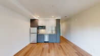 Located at 1341 N Killingsworth St in Portland, Oregon, this thoughtfully designed studio offers a clean, modern aesthetic across a single level. Light-toned hardwood flooring runs throughout, lending warmth and visual continuity to the entire space.

The open living area is bright and inviting, anchored by a glass-paneled door that opens onto a private balcony with views of the surrounding neighborhood. Flanking windows invite generous natural light, enhancing the airy feel of the room.

The kitchen is efficiently appointed with two-tone cabinetry — pairing grey lower cabinets with white upper cabinets — complemented by a white subway tile backsplash and stainless steel appliances, including a refrigerator, microwave, dishwasher, and cooktop. Recessed lighting above the kitchen adds a polished touch.

A dedicated niche along the hallway houses a full-size stacked washer and dryer unit, providing the convenience of in-unit laundry. The bathroom features a sleek grey vanity with an undermount sink, a large mirror, and continued hardwood-style flooring, maintaining the contemporary design language found throughout the unit.

Clean white walls and a neutral palette create a versatile backdrop, making this space well-suited for efficient, modern urban living in North Portland.