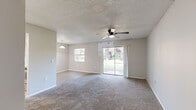 This single-floor, 1-bedroom, 1-bathroom unit offers a practical and comfortable layout across a compact yet efficient footprint. The combined kitchen and living room serves as the heart of the space, where the living area features plush carpeted flooring, a ceiling fan with light fixture, and a full-width sliding glass door that floods the room with natural light and provides direct views of a lush, tree-lined outdoor setting. Adjacent to the living area, a pendant light marks the dining zone, which transitions seamlessly via light wood-look flooring into the kitchen. The kitchen is equipped with white shaker cabinetry, stone-look countertops, stainless steel appliances including a refrigerator, dishwasher, and range, as well as a double-basin sink. A pass-through counter with a stone-look surface connects the kitchen to the living and dining area, enhancing the open feel. The bedroom offers carpeted flooring, a double sliding-door closet, a ceiling fan, and a window with outdoor views. The bathroom features a full tub-shower combo with white tile surround, a vanity with stone-look countertop, and light wood-look tile flooring. A hallway connects the private and common areas of the unit.