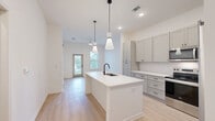 Located at 100 Wilton Cir S in Palm Coast, Florida, this thoughtfully designed one-bedroom, one-bathroom home offers an efficient and modern single-floor layout. The open-concept living area seamlessly integrates the kitchen, dining, and living spaces, creating a bright and welcoming environment filled with natural light.

The kitchen is a standout feature, showcasing gray shaker-style cabinetry, a classic white subway tile backsplash, light quartz countertops, and a central island with an undermount sink and matte black faucet. Stainless steel appliances — including a French door refrigerator, electric range, and over-the-range microwave — complete the well-appointed cooking space. Stylish pendant lights hang above the island, adding a contemporary design touch alongside recessed ceiling lighting throughout.

Light wood-look flooring runs continuously across the entire home, contributing to a cohesive and airy aesthetic. The bedroom is a comfortable, well-lit retreat with a window that brings in natural light. The full bathroom features gray cabinetry with a quartz vanity top, an undermount sink, matte black fixtures, and a lighted mirror. Two closets and a dedicated laundry area provide practical storage and utility solutions. The home's clean, neutral palette and modern finishes make for a move-in ready living space.