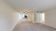 This single-story residence offers a thoughtfully arranged floor plan with a comfortable, functional layout throughout. The spacious living area serves as the heart of the home, featuring neutral-toned carpet, a ceiling fan with light fixture, and an open sightline to the kitchen. Built-in shelving adds a practical storage element adjacent to the kitchen pass-through, which enhances connectivity between the living and cooking spaces.

The kitchen is well-appointed with crisp white shaker-style cabinetry extending to the ceiling, a classic subway tile backsplash, wood-look flooring, a double-basin stainless steel sink, and black appliances including a range, microwave, and refrigerator. A breakfast bar provides a convenient casual dining option.

The bedrooms are carpeted and finished with neutral gray walls, each featuring windows with blinds that allow natural light and views of the surrounding greenery. The rooms offer a clean, versatile canvas suitable for various configurations.

Two full bathrooms are present in the unit. Both feature white tiled tub-and-shower combinations with brushed nickel or gold-tone fixtures, white vanities, and one includes wood-look vinyl flooring. The overall aesthetic is clean, bright, and move-in ready.