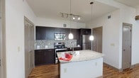 This single-floor, 1-bedroom, 1-bathroom residence offers a thoughtfully designed layout with contemporary finishes throughout. The open-concept kitchen serves as the centerpiece of the living area, showcasing dark espresso cabinetry, granite countertops, a mosaic tile backsplash, and a full suite of stainless steel appliances including a range, microwave, and refrigerator. A large kitchen island with an undermount sink and pendant lighting above adds both functionality and style, while a track lighting system illuminates the space. Wood-style flooring runs consistently throughout the main living areas, lending warmth and cohesion to the design. The bedroom offers a clean, neutral palette with ample natural light and direct access to a spacious walk-in closet outfitted with wire shelving systems on three walls, providing generous storage. The bathroom continues the upscale design language with dark cabinetry, a granite vanity top, an undermount sink, a framed mirror, and a tall linen tower cabinet for additional storage. Wood-style flooring carries into the bathroom as well. The overall ambiance of the unit is modern and clean, with a neutral color scheme and quality finishes that create a polished, move-in-ready living environment.