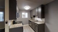 This single-floor space offers a clean, modern aesthetic highlighted by a thoughtfully designed kitchen. The kitchen features dark charcoal cabinetry that extends from floor to ceiling, providing generous storage throughout. Granite-style countertops in a neutral tone complement the cabinetry and offer ample prep space. Stainless steel appliances, including a range, dishwasher, and built-in microwave, lend a sleek, contemporary feel. A double-basin stainless steel sink is positioned beneath a window that invites natural light into the space, brightening the room and creating an open atmosphere. Light wood-look flooring runs throughout, offering a warm contrast to the darker cabinetry. The walls are finished in a soft neutral gray, contributing to a cohesive and modern color palette. A flush-mount ceiling light provides consistent overhead illumination. The textured ceiling adds a subtle detail to the overall finish of the space. The galley-style layout of the kitchen is efficient and functional, making excellent use of the available space while maintaining a tidy, organized appearance. Overall, the space presents a polished, updated interior with practical design choices throughout.