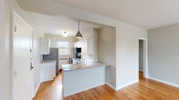 This well-appointed 2-bedroom, 1-bathroom unit in Detroit, MI offers a thoughtfully designed single-floor layout with warm hardwood flooring flowing throughout. The open kitchen is a standout feature, showcasing white shaker cabinetry, a classic subway tile backsplash, granite countertops, and a full suite of stainless steel appliances including a range, microwave, dishwasher, and refrigerator. A peninsula with additional granite counter space connects the kitchen to the adjacent living area, creating an open, functional flow. Industrial-style pendant lighting adds a modern accent above the workspace. The living room offers generous open space filled with natural light, while the two bedrooms provide comfortable, well-proportioned retreats — each with hardwood floors, neutral tones, and natural light from windows. The primary bedroom includes a dedicated closet with built-in shelving. The bathroom features a tub-shower combination, white tiled walls with classic navy accent tiles, a patterned tile floor, and a window for natural ventilation. Additional storage closets and a defined hallway and entrance complete the practical layout of this clean, move-in-ready unit.