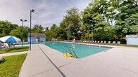 Located at 2500 Knights Rd in Bensalem, PA, this 3-floor residential community offers an impressive array of outdoor amenities set against a backdrop of lush, mature trees and well-maintained green spaces. The grounds are thoughtfully designed to encourage an active and social lifestyle.

At the heart of the outdoor area is a large swimming pool with a wide surrounding deck lined with lounge chairs, a lifeguard station, and a poolside utility building — ideal for warm-weather recreation. Adjacent to the pool, a spacious hot tub area provides a quieter relaxation option, also surrounded by seating along manicured lawns.

For active residents, the community features multi-use sport courts with clearly marked lines for basketball and other court sports, finished in vibrant blue and green surfaces. The courts are enclosed by chain-link fencing and shaded by surrounding trees.

A dedicated picnic area offers multiple wooden picnic tables spread across a grassy, tree-shaded lawn, accessible via steps from an upper level — perfect for outdoor gatherings. A fenced dog park with agility features provides a safe and engaging space for pets.

The broader grounds include open lawn areas, established trees, and views of the brick residential buildings, all contributing to a welcoming, community-oriented atmosphere throughout the property.