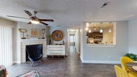 This single-floor residence offers a cohesive and thoughtfully designed layout that balances functionality with contemporary style. Dark hardwood-style flooring flows consistently throughout the space, creating a unified aesthetic across all rooms. The living area features a classic fireplace with a white tile surround, a ceiling fan, and a textured ceiling, establishing a comfortable and welcoming atmosphere. Adjacent to the living room, the compact kitchen is outfitted with dark cabinetry, stainless steel appliances including a range and microwave, and a clean white subway tile backsplash. A pass-through opening connects the kitchen to the dining area, which provides a cozy setting for meals. The dedicated dining space is bright and well-defined, ideal for everyday use. A hallway leads to the private quarters, which include a spacious primary bedroom with its own exterior-facing door and a ceiling fan, as well as a secondary bedroom that benefits from natural light through a window and includes space for a desk. Both bedrooms feature textured ceilings and ceiling fans. The two full bathrooms are finished with dark vanity cabinetry, white countertops, tiled tub-shower combinations, and wood-look flooring, offering a consistent and clean design throughout.