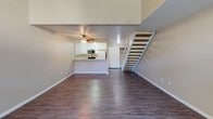 Located at 1327 Deerpark Dr in Fullerton, California, this two-story residence offers a thoughtfully designed layout across two levels. The main floor greets you with a generous open-concept living area finished with rich hardwood-style flooring that extends throughout. Exposed wood beam accents on the ceiling add a touch of character, while a wall-unit air conditioner and sliding glass door leading to a covered outdoor patio provide both comfort and connectivity to the outdoors. The kitchen is open to the living space via a peninsula-style counter, and features white cabinetry, a stainless steel electric range, built-in microwave, and a white refrigerator — all set beneath dedicated overhead lighting. A staircase with white railings and wood-toned steps connects the main floor to the upper level. Upstairs, the primary bedroom is carpeted for warmth and comfort, fitted with a ceiling fan, and opens directly to a vanity area with cabinetry and a mirror. The bathroom is equipped with a tub and shower combination enclosed by sliding frosted glass doors, along with a wall-mounted grab bar for added accessibility. Clean, neutral wall tones are maintained throughout the home, creating a bright and cohesive aesthetic across both floors.