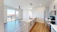 Located at 700 Semmes Ave in Richmond, Virginia, this thoughtfully designed 2-bedroom, 2-bathroom residence offers a clean, modern aesthetic throughout. The open-concept layout seamlessly connects the kitchen and living area, where warm hardwood-style flooring and crisp white walls create a bright, welcoming atmosphere. Large windows and a sliding glass door flood the space with natural light and lead to a private balcony with expansive views of the Richmond skyline.

The contemporary kitchen is a standout feature, anchored by a generous island with a white quartz countertop, undermount sink, and matte black fixtures. Light gray flat-front cabinetry, a white subway tile backsplash, and stainless steel appliances complete the polished look. A modern linear pendant light adds a stylish focal point overhead.

The primary bedroom is a comfortable retreat with large windows framing city views, warm hardwood floors, and a dedicated ceiling fan. A well-proportioned closet provides ample storage. The second bedroom also enjoys generous natural light and hardwood flooring.

Both bathrooms are finished with clean, modern detailing. The primary bath features a dual-sink vanity with white quartz countertops, matte black hardware, and sleek vertical sconce lighting. The second bath mirrors the same refined aesthetic with an undermount sink and contemporary fixtures throughout.