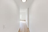 Located at 1030 Post St in San Francisco's Polk Gulch neighborhood, this two-bedroom, one-bathroom residence offers a clean and minimalist aesthetic throughout its single-floor layout. The interior is defined by crisp white walls and light hardwood flooring that runs through the main living areas and hallways, creating a bright and cohesive feel.

The living area is open and airy, with a large window that allows natural light to pour in and offers views of the surrounding cityscape. It connects seamlessly to the compact kitchen, which features white shaker-style cabinetry, marble-patterned countertops, a stainless steel sink, and white appliances including a coil-top range and refrigerator.

The spacious primary bedroom is carpeted and bathed in natural light from generously sized windows with city views. Distinctive angled architectural elements add character to the room. The second bedroom similarly benefits from natural light and a bright, neutral palette.

Two hallways connect the rooms efficiently, maintaining a logical and functional flow. The bathroom is neatly appointed with a white vanity, mirrored medicine cabinet, a tub-shower combination, and wood-toned flooring. Flush-mount lighting fixtures and baseboard heating are present throughout the unit, contributing to a practical and comfortable living environment.