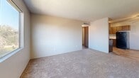 Located at 2430 N Dodge Blvd in Tucson, Arizona, this single-floor unit offers a practical and well-organized layout across two bedrooms, one bathroom, a living room, kitchen, and hallway. The kitchen features warm-toned wood cabinetry with ample upper and lower storage, light-colored countertops, a double stainless steel sink, and black appliances including an electric range and refrigerator. Wood-look flooring runs throughout the kitchen and dining area, which is accented by a ceiling fan overhead. The open living area flows naturally from the kitchen and is finished with plush carpet and a textured ceiling. Both bedrooms are carpeted and receive natural light through sliding windows that offer views of surrounding greenery and palm trees. The primary bedroom is a comfortable size and includes a closet with bifold doors. The bathroom is cleanly appointed with a full tub-shower combination featuring white tile surround, a vanity with a speckled countertop, and wood-look flooring. A hallway connects the main living areas to the bedrooms, with HVAC vents providing climate control throughout. The textured ceilings are consistent across the unit, contributing to a cohesive interior character.