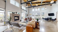 Located at 825 Cleveland Ave in Columbus, Ohio, The Rise is a thoughtfully designed community clubhouse that blends industrial architecture with warm, contemporary interiors. The space is anchored by a striking reception desk crafted from natural wood planks, set beneath a sculptural woven pendant light, with bold "THE RISE" signage making an immediate impression upon entry.

The main lounge area is a showstopper, boasting soaring ceilings with exposed steel beams and warm wood decking overhead. A floor-to-ceiling brick fireplace serves as the focal point, flanked by a curated mix of seating including a plush sectional, leather accent chairs, and sleek modern furnishings. Industrial-style pendant lights hang throughout, complementing the polished concrete floors that flow seamlessly across the entire space.

Oversized windows and full-height garage-style glass doors flood the interior with natural light and offer direct views and access to an outdoor patio area. A dedicated dining and co-working zone features bar-height seating along the windows, perfect for casual work or socializing.

The fully equipped kitchen includes modern cabinetry, a large island with bar seating, stainless appliances, and a wall-mounted TV. A separate refreshment station with a coffee setup serves the entryway area. A comfortable waiting lounge near the reception completes this well-appointed, multifunctional community hub.