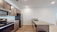 Located at 321 E Park Rd in Indian Trail, NC, this single-story residence offers a well-designed layout with clean, contemporary finishes throughout. The kitchen is a standout feature, outfitted with rich dark brown shaker-style cabinetry, granite-look countertops, and a full suite of stainless steel appliances including a refrigerator, electric range, and over-the-range microwave. A kitchen island with an integrated sink adds functional workspace, while durable wood-look flooring anchors the entire cooking and dining area. The open living room is generously proportioned, bathed in natural light through large windows fitted with blinds, and finished with plush neutral carpeting and crown molding that lend a polished feel. Multiple bedrooms continue the carpeted aesthetic, each offering windows for natural light and ample wall space. The bathrooms feature wood-look tile flooring, full tub-and-shower combinations with brushed nickel fixtures, and vanities with dark cabinetry. A walk-in closet with wire shelving provides convenient storage off one of the bathrooms. Throughout the home, recessed lighting, crisp white walls, and consistent trim work create a bright, cohesive atmosphere well-suited for comfortable everyday living.