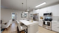 Located at 3795 Bismarck Ct in Oxford, Florida, this single-story residence presents a cohesive modern design throughout its well-appointed interior. The open-concept kitchen serves as a central highlight, featuring crisp white shaker cabinetry, a classic subway tile backsplash, and a full suite of stainless steel appliances including a French door refrigerator, electric range, and over-the-range microwave. A central island with a white quartz countertop, undermount sink, and bar seating is illuminated by brushed nickel pendant lights, creating a natural gathering space. Light wood-style flooring runs through the kitchen and living areas, contributing to the home's bright, airy feel.

The living room offers access to the outdoors through glass panel doors, allowing natural light to filter in alongside views of the surrounding landscape. Multiple bedrooms provide comfortable retreats, finished with plush carpeting, large windows dressed with soft drapery, and ample space for furnishings. The bathrooms are well-designed, featuring white vanities with quartz countertops, wood-look tile flooring, subway tile shower surrounds, and a frameless sliding glass shower door in the primary bath. A dedicated laundry room with full-size washer and dryer with overhead shelving completes the practical layout of this thoughtfully designed residence.