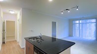 Located at 890 S Matlack Street in West Chester, PA, this single-floor residence offers a clean, modern aesthetic with an open-concept design that maximizes both functionality and flow. The kitchen serves as a focal point of the living space, anchored by a large center island finished with a striking dark granite countertop and an undermount stainless steel sink. Warm-toned wood cabinetry adds contrast against the light walls, while an integrated dishwasher contributes to the seamless, streamlined look. Overhead, a track lighting system provides adjustable, directional illumination to complement the recessed lighting throughout. The kitchen opens directly into a spacious living area, creating an expansive, connected feel ideal for everyday living and entertaining. Light-toned flooring runs through the main living space, while plush carpeting carries into the adjoining room visible through a centered doorway. Vertical blinds on a large window allow for flexible natural light control, brightening the space while maintaining privacy. Crown molding details along the ceiling add a refined architectural touch. The overall ambiance is contemporary and well-appointed, reflecting thoughtful design choices throughout.