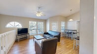 Located at Riviera, this single-floor unit offers a well-designed layout that balances comfort and functionality. The open-concept living area is bathed in natural light streaming through multiple large windows fitted with white blinds, creating a bright and welcoming atmosphere. A ceiling fan overhead and warm hardwood-style flooring running throughout the space add to the inviting ambiance. The living room is furnished with a leather sofa and armchair, a flat-screen TV, and a coffee table, while a charming arched accent window adds architectural character to the space.

Adjacent to the living area, the dining space features a raised bar-height table with stylish metal-framed chairs and is illuminated by a pendant light, with direct access to an outdoor area via a glass-panel door. The kitchen is well-appointed with granite countertops, white cabinetry, a stainless steel sink, and black appliances including an electric range and over-the-range microwave, along with ample storage provided by a spacious closet pantry.

The bedroom offers a comfortable retreat with a ceiling fan, a large closet with double doors, and a window that lets in natural light. The full bathroom is clean and functional, featuring a tiled tub-shower combo, a granite-topped vanity with white cabinetry, and hardwood-style flooring.