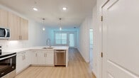 Located at 1305 Farkleberry Ln in Davenport, FL, this thoughtfully designed one-bedroom, two-bathroom residence offers a clean, modern aesthetic defined by bright white walls, light wood-look flooring, and contemporary finishes throughout. The open-concept kitchen and living area serves as the heart of the home, anchored by a sleek peninsula with a undermount sink and pendant lighting above. The kitchen is well-appointed with light wood and white cabinetry, white quartz countertops, and a full suite of stainless steel appliances including a French door refrigerator, electric range, and over-the-range microwave. The living area benefits from natural light streaming through large windows fitted with horizontal blinds and provides access to an outdoor area via a glass-paned door. The spacious primary bedroom features a ceiling fan, a generous walk-in closet, and its own natural light from a window overlooking the outdoors. Two bathrooms are finished with light wood floating vanities, white quartz countertops, large mirrors, and wood-look flooring. One bathroom includes a soaking tub with tiled surround. The overall ambiance is bright, clean, and move-in ready, reflecting a cohesive modern design sensibility.