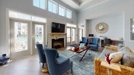 Located in Goose Creek, South Carolina, the Crowfield Reserve clubhouse is a thoughtfully designed single-story amenity space that blends comfort with functionality. The lounge area serves as the heart of the space, boasting soaring double-height ceilings lined with expansive transom windows that flood the room with abundant natural light. A shiplap-clad fireplace anchors the living area, framed by French doors that open to outdoor views of the surrounding community. Elegant blue wingback chairs, a tray ceiling with crown molding, and warm hardwood flooring complete the inviting atmosphere. The kitchen is outfitted with floor-to-ceiling gray shaker cabinets, quartz countertops, a light blue glass tile backsplash, and stainless steel appliances, including a side-by-side refrigerator — offering generous prep and storage space. The fitness center is a standout feature, occupying a spacious area with a tray ceiling, ceiling fan, and large windows providing natural light. It is fully equipped with strength machines, free weights, medicine balls, spinning bikes, cardio equipment, and a wall-mounted television, all set on stylish teal and gray interlocking floor tiles. Together, these spaces create a welcoming and well-appointed community hub.