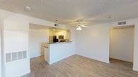 This single-floor residence offers a clean, open-concept layout designed for comfortable everyday living. The living area features light wood-style flooring that runs throughout, creating a warm and cohesive aesthetic. A ceiling fan with a light fixture is centrally positioned, adding both function and a finishing touch to the space.

The kitchen is accessible via a peninsula-style breakfast bar topped with granite countertops, providing a natural divide between the cooking and living areas while maintaining an open feel. White cabinetry lines the kitchen walls, offering ample storage, while stainless steel appliances — including a refrigerator, microwave, and range — add a modern, polished look. Recessed lighting above the kitchen workspace ensures the area is well-lit.

The textured popcorn ceilings are consistent throughout the space, and crisp white walls provide a neutral backdrop that allows for versatile interior styling. HVAC vents are integrated into the ceiling, ensuring efficient climate control. The overall ambiance is bright, clean, and functional, making this a well-appointed space suited for a variety of lifestyles.