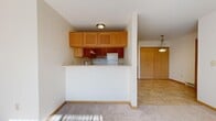 This single-floor residence offers a thoughtfully designed layout filled with abundant natural light throughout. The kitchen is a functional centerpiece, featuring rich cherry-toned cabinetry extending to the ceiling, light-colored countertops, hardwood-style flooring, and a full suite of black appliances including a refrigerator, range, over-the-range microwave, and dishwasher. A pantry or storage closet is conveniently located adjacent to the kitchen area.

The living space is defined by plush, neutral-toned carpeting and is separated from the kitchen area by a half-wall partition, creating a natural division while maintaining an open feel. A standout architectural detail is the elegant French door with multi-pane glass panels, which opens to an outdoor balcony and allows generous natural light to pour into the room. An arched window further enhances the brightness of the space.

The bedrooms are carpeted and well-lit, each featuring large multi-pane windows that frame outdoor views of surrounding greenery and neighborhood scenery. Sliding and hinged closets with built-in wire shelving provide practical storage solutions in the sleeping quarters.

The bathroom is clean and efficiently designed, featuring a full soaking tub with a tiled surround and shower combination, complemented by light tile flooring. Throughout the residence, a consistent warm neutral palette and ample window placement create a welcoming and light-filled atmosphere.