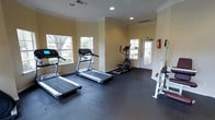 This single-floor fitness center is designed to provide a practical and welcoming environment for residents or members to meet their exercise needs. The space is finished with durable dark rubber flooring, ideal for high-traffic workout use, and features warm yellow-toned walls accented by elegant crown molding that add a polished touch to the room.

Natural light flows generously into the space through multiple windows, offering pleasant outdoor views of surrounding greenery that create a refreshing atmosphere during workouts. Recessed lighting in the ceiling ensures the room remains well-lit throughout the day.

The cardio area is well-appointed with two treadmills and an elliptical machine, all positioned near the windows to take advantage of the natural light and outdoor views. A strength training station is also available on the opposite side of the room, providing options for a full-body workout routine.

A glass-panel door offers direct access to an outdoor area, enhancing ventilation and connectivity to the exterior. Safety is also addressed with a fire extinguisher mounted near the exit. Overall, this fitness center strikes a balance between functionality and comfort, making it a convenient and well-maintained space for staying active.