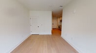 This contemporary single-floor space combines clean design with functional living. Light-toned hardwood flooring flows consistently throughout, creating a cohesive and airy atmosphere across all rooms.

The open living area is bright and minimalist, framed by crisp white walls and recessed lighting. A louvered door provides access to a closet, while the layout opens naturally toward the kitchen.

The kitchen is a standout feature, designed with a galley-style configuration that maximizes efficiency. High-gloss white cabinetry extends floor to ceiling, complemented by a classic white subway tile backsplash and sleek grey countertops. Stainless steel appliances — including a range, built-in microwave, dishwasher, and full-size refrigerator — complete the modern culinary setup.

The bedroom is a tranquil retreat, defined by a large multi-pane window fitted with roller shades that frames views of the surrounding brick urban streetscape. Recessed lighting and continued hardwood flooring maintain the unit's consistent aesthetic.

The bathroom features a frameless glass-enclosed walk-in shower dressed in white horizontal tile, chrome fixtures, and hexagonal mosaic floor tile, all contributing to a clean, spa-like feel.

Overall, the space presents a polished, contemporary design with quality finishes throughout.