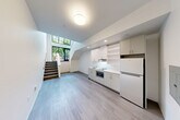 Located at 312 W Republican St in Seattle's desirable Queen Anne neighborhood, this modern two-story residence offers a thoughtfully designed layout spread across two floors. The main level is anchored by a bright, open-plan kitchen and living area featuring light hardwood-style flooring, crisp white walls, and sleek white cabinetry with ample open shelving. A full suite of appliances, including a refrigerator and built-in microwave, keeps the kitchen functional and efficient. Large black-framed windows flood the space with natural light and frame views of the lush, tree-lined streetscape. A striking staircase with a modern cable railing connects the floors, adding an architectural focal point and a sense of vertical openness. The upper level hosts the private bedroom, complete with a window overlooking the greenery outside, and connects to a well-appointed bathroom featuring a white vanity with generous counter space and a large mirror. A second bathroom and a dedicated laundry area add everyday convenience. Outside, a paved patio with warm wood-slatted fencing and landscaped planters provides a welcoming outdoor retreat that opens to the vibrant neighborhood surroundings. Clean lines and a neutral palette throughout give the space a contemporary, move-in-ready feel.