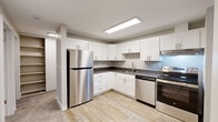 Located in Tacoma, WA, this two-bedroom, one-bathroom residence offers a well-organized single-floor layout designed for comfortable everyday living. The updated kitchen is a standout feature, showcasing white shaker cabinetry with brushed nickel hardware, dark stone-look countertops, light wood-style flooring, and a full suite of stainless steel appliances including a refrigerator, electric range, and dishwasher. A skylight-style ceiling fixture provides bright overhead illumination throughout the cooking space. The open living room is carpeted and anchored by a classic fireplace with a dark surround, while sliding glass doors lead to a private balcony with outdoor views of surrounding greenery. Both bedrooms are carpeted and receive natural light through large windows overlooking mature trees. Baseboard heating units are present throughout. The bathroom features wood-style flooring, a full tub-shower combination with clean white surround, and brushed nickel fixtures and accessories. A dedicated laundry area houses a stacked washer and dryer unit, adding everyday convenience. A utility room and closet storage round out the functional layout of this thoughtfully appointed residence.