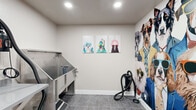 Located at 2727 Edison St in San Mateo, CA, this purpose-built pet grooming room is a well-appointed, single-floor space designed entirely with pet care in mind. The room centers around a professional-grade stainless steel dog bathing tub, complete with an integrated ramp for easy pet access, a coiled hose, and water fixtures — all built for efficient and comfortable grooming sessions. Opposite the tub, a built-in gray countertop provides a dedicated prep and supply area, offering ample workspace for grooming tools, towels, and accessories. Hooks mounted near the entry door conveniently hold grooming aprons, keeping essentials within easy reach. The flooring throughout consists of durable gray tile, practical for a wet-use environment and easy to maintain. The space is elevated by its distinctive decor: a large, colorful mural of stylishly dressed dogs wearing sunglasses commands one full wall, while framed whimsical dog portrait prints add personality to the remaining walls. A fire extinguisher and safety signage are also present, reflecting attention to safety standards. The overall ambiance is clean, functional, and cheerfully themed — making it an inviting and practical environment for pet grooming at this San Mateo address.