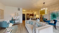 Located at 11130 N Buntrock Ave in Mequon, Wisconsin, this refined single-floor residence showcases a thoughtfully designed open-concept layout that seamlessly connects the living, dining, and kitchen areas. Light hardwood flooring flows throughout the main living spaces, complementing the bright, neutral palette and creating a warm, cohesive atmosphere.

The expansive living area is anchored by large floor-to-ceiling windows that bathe the room in natural light and offer serene views of the surrounding greenery, with access to an outdoor balcony. A statement chandelier adds a touch of elegance overhead.

The gourmet kitchen is appointed with rich dark cabinetry, stainless steel appliances, a large center island with a light quartz countertop, and stylish pendant lighting — ideal for both everyday cooking and entertaining. An adjacent dining area, framed by a sliding glass door to the balcony, provides a bright and inviting setting.

The primary bedroom is a tranquil retreat featuring plush carpeting, multiple windows with wooded views, a decorative chandelier, and ample space for a full furniture suite. The en-suite bathroom offers a walk-in glass shower, dark wood vanity with a quartz countertop, and elegant tile flooring, delivering a spa-like experience.